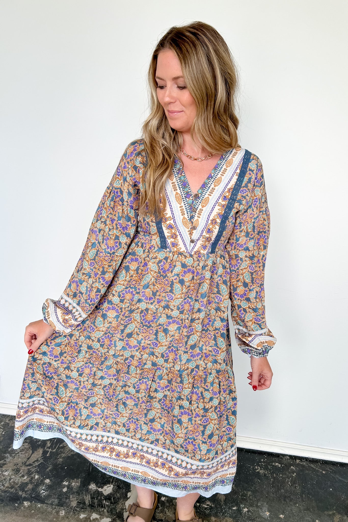 Woman wearing a long floral dress against a white wall