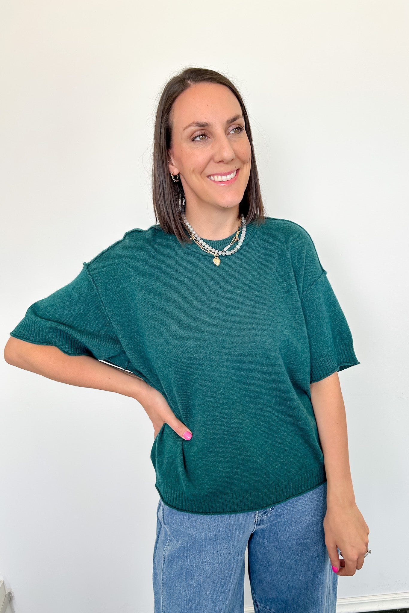 Woman wearing a green sweater and blue jeans against a white background