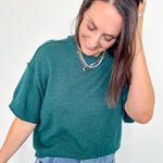 Woman wearing a teal sweater and blue jeans against a white background
