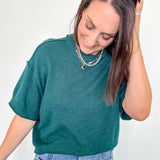 Woman wearing a teal sweater and blue jeans against a white background