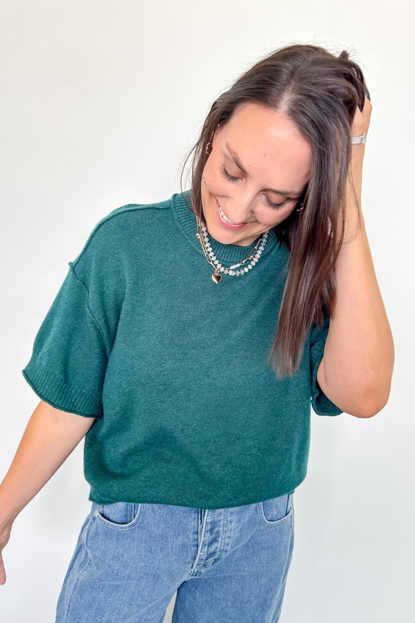Woman wearing a teal sweater and blue jeans against a white background
