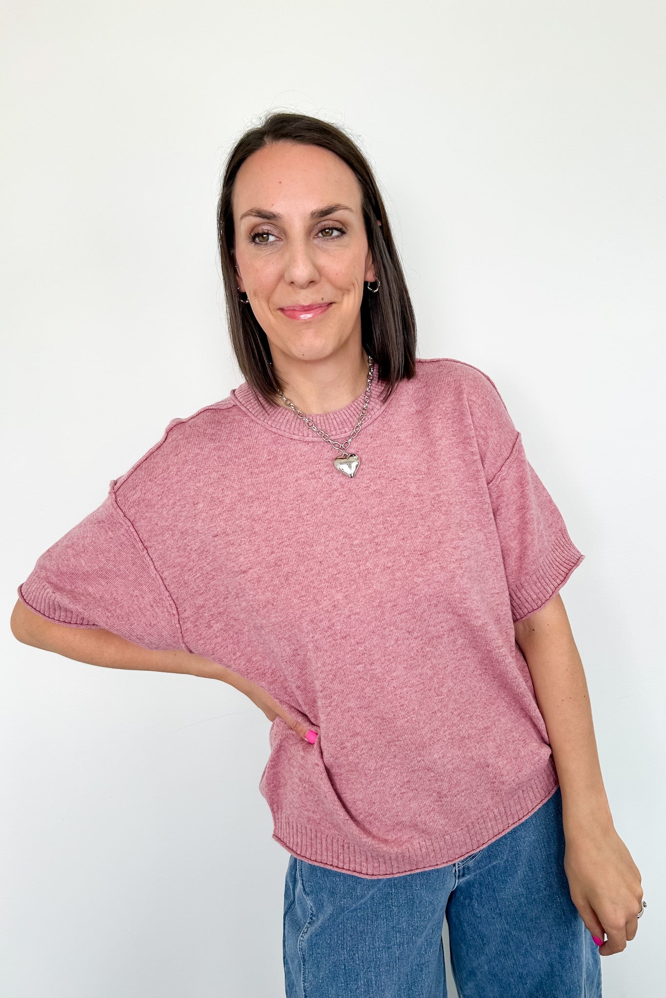 Woman wearing a pink sweater and blue jeans against a white background