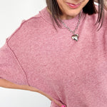 Woman wearing a pink sweater with a heart-shaped pendant on a white background