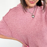 Woman wearing a pink sweater with a heart-shaped pendant on a white background