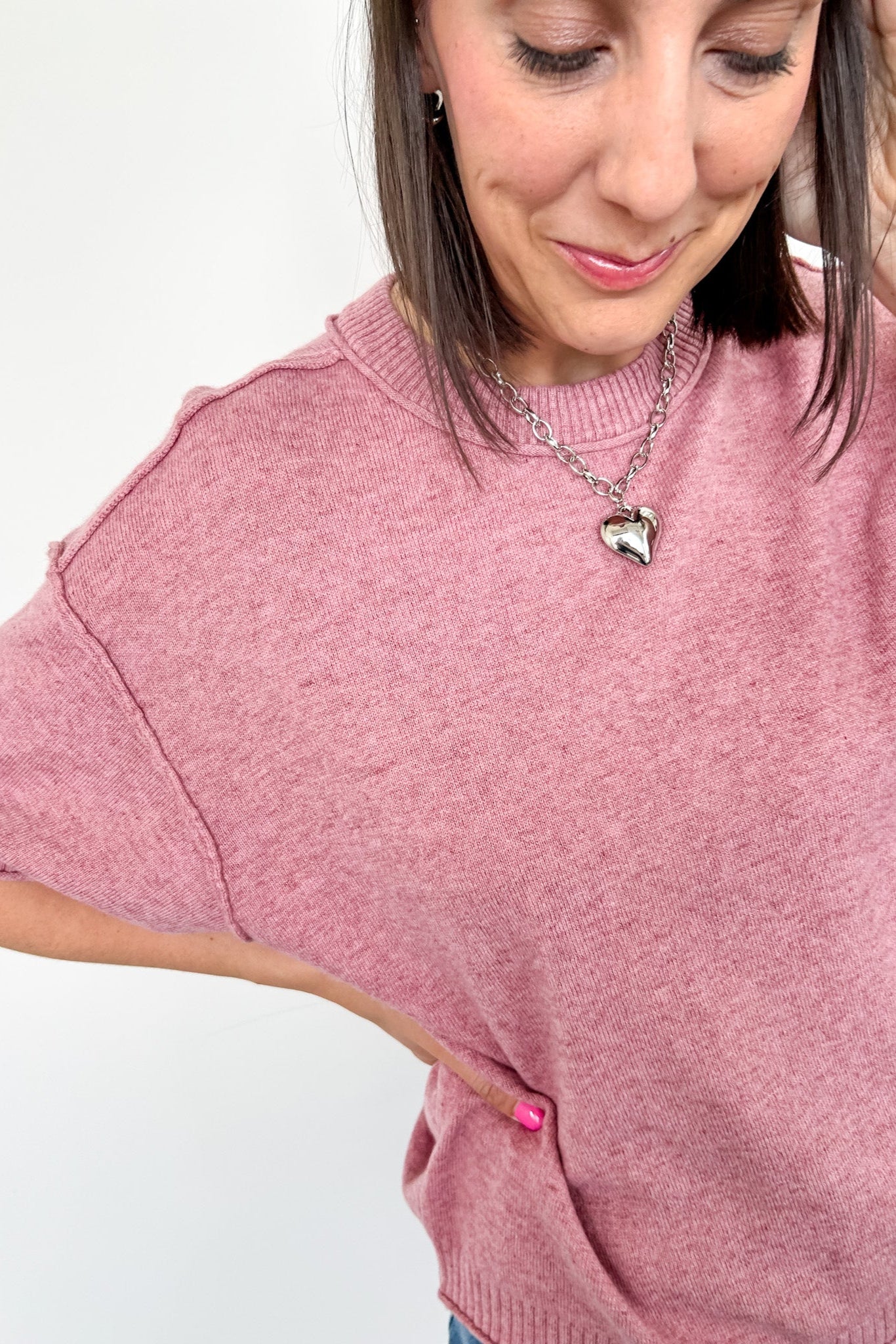 Woman wearing a pink sweater with a heart-shaped pendant on a white background