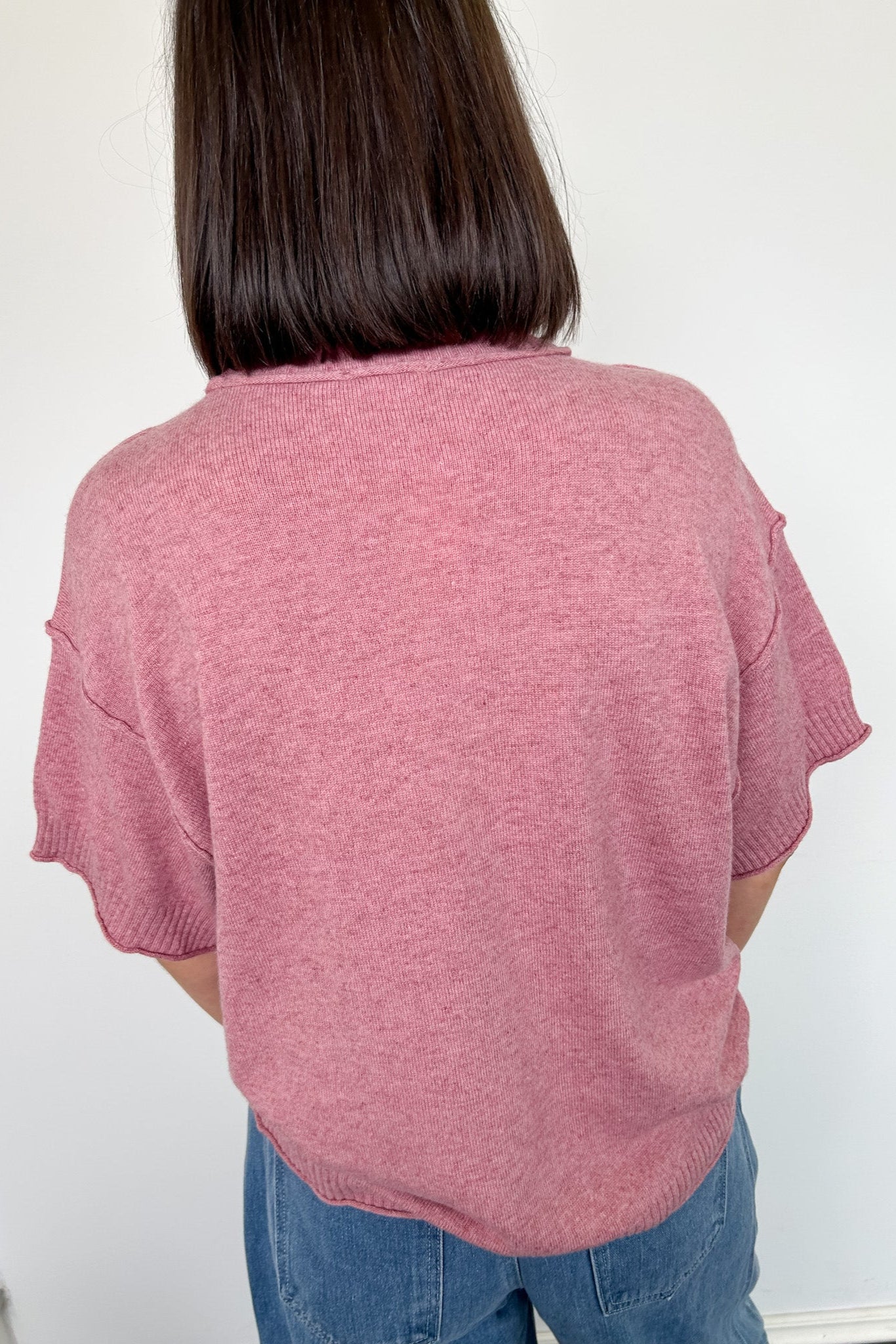 Person wearing a pink sweater and blue jeans against a white background