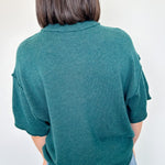 Person wearing a teal sweater and blue jeans against a white wall