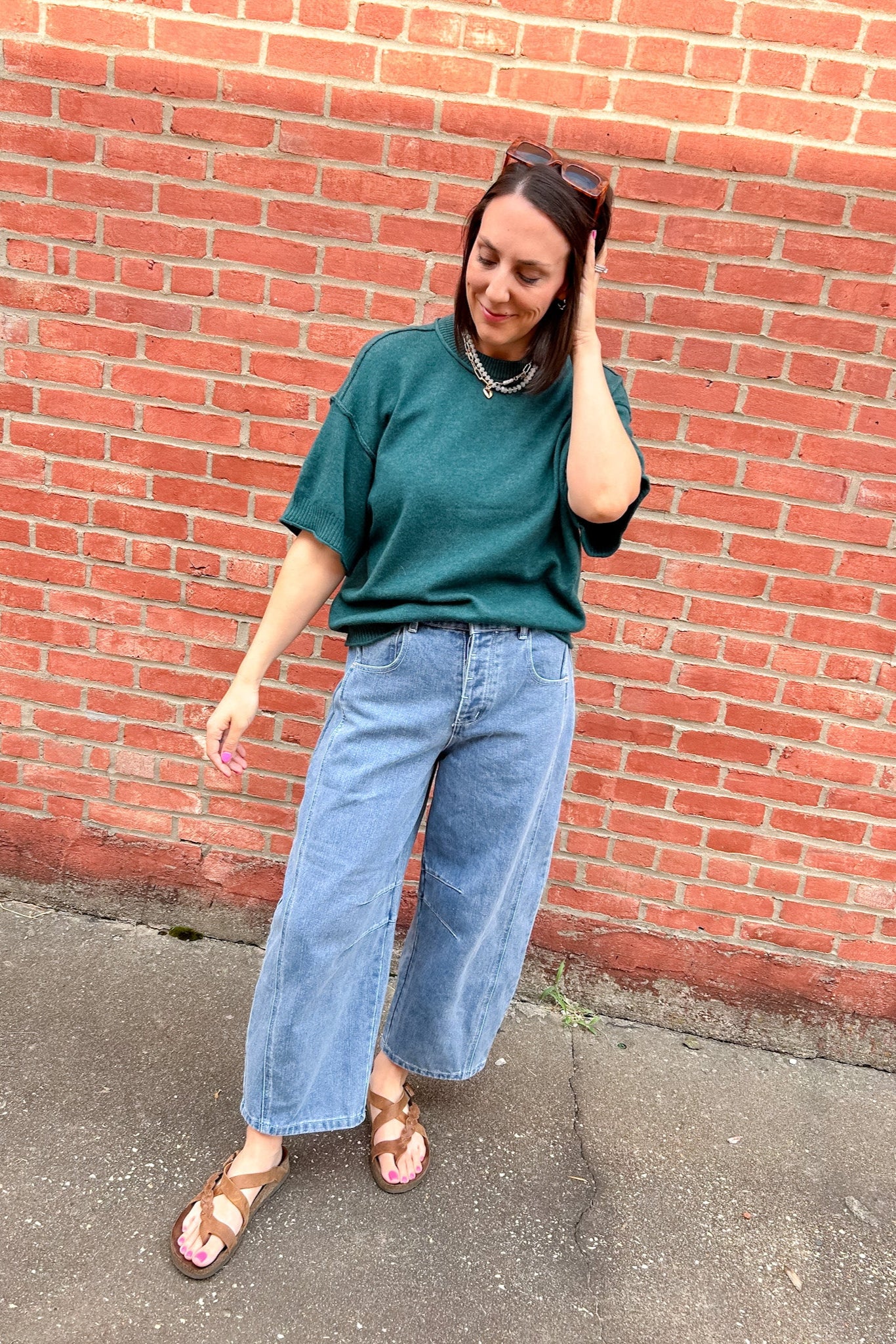 Person wearing a green shirt and blue jeans standing against a red brick wall.