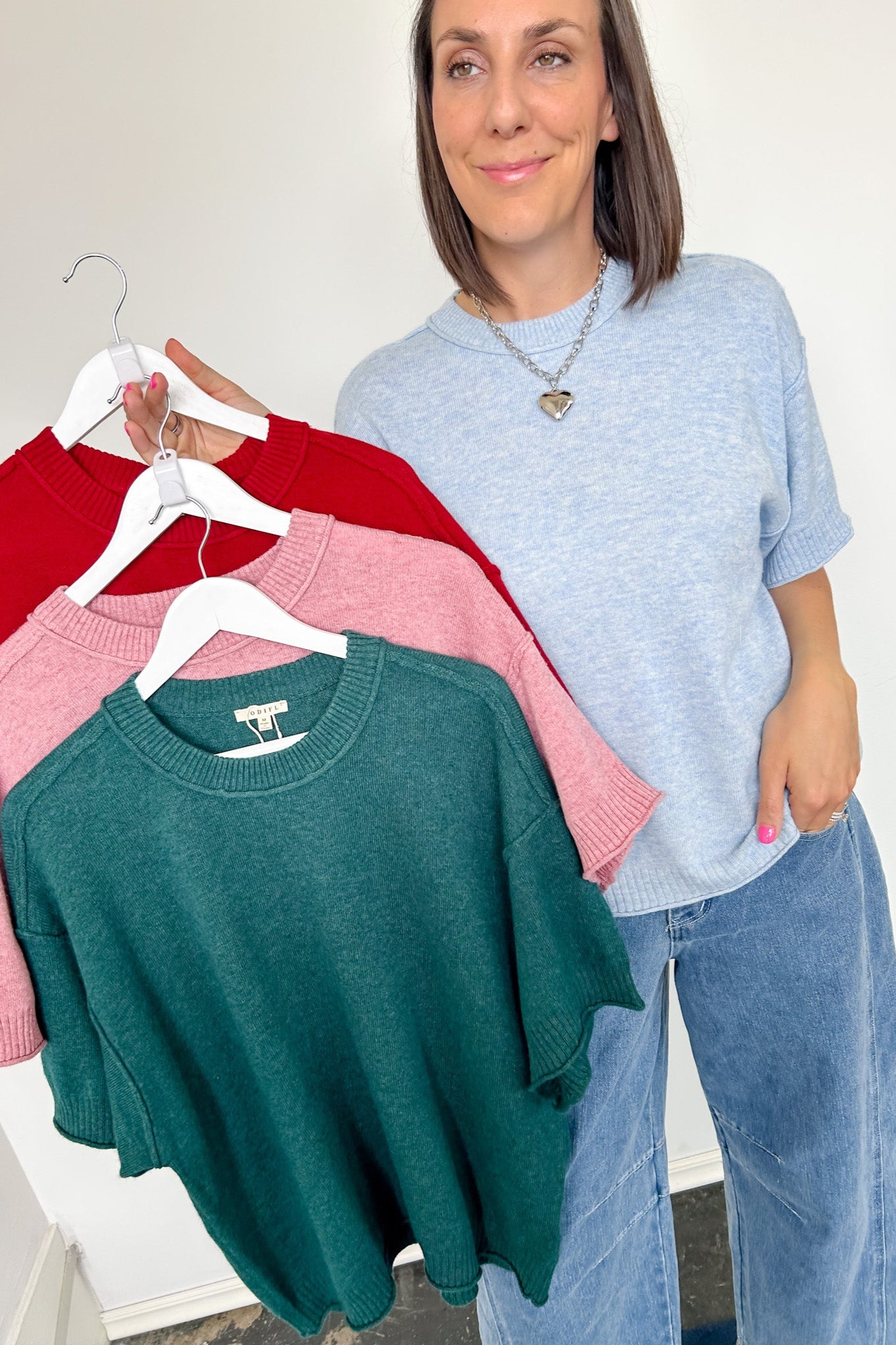 Woman holding a rack of sweaters in red, pink, and green.