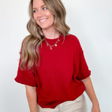 Woman wearing a red top and beige pants against a white background