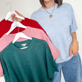 Woman holding a rack of sweaters in red, pink, and green.