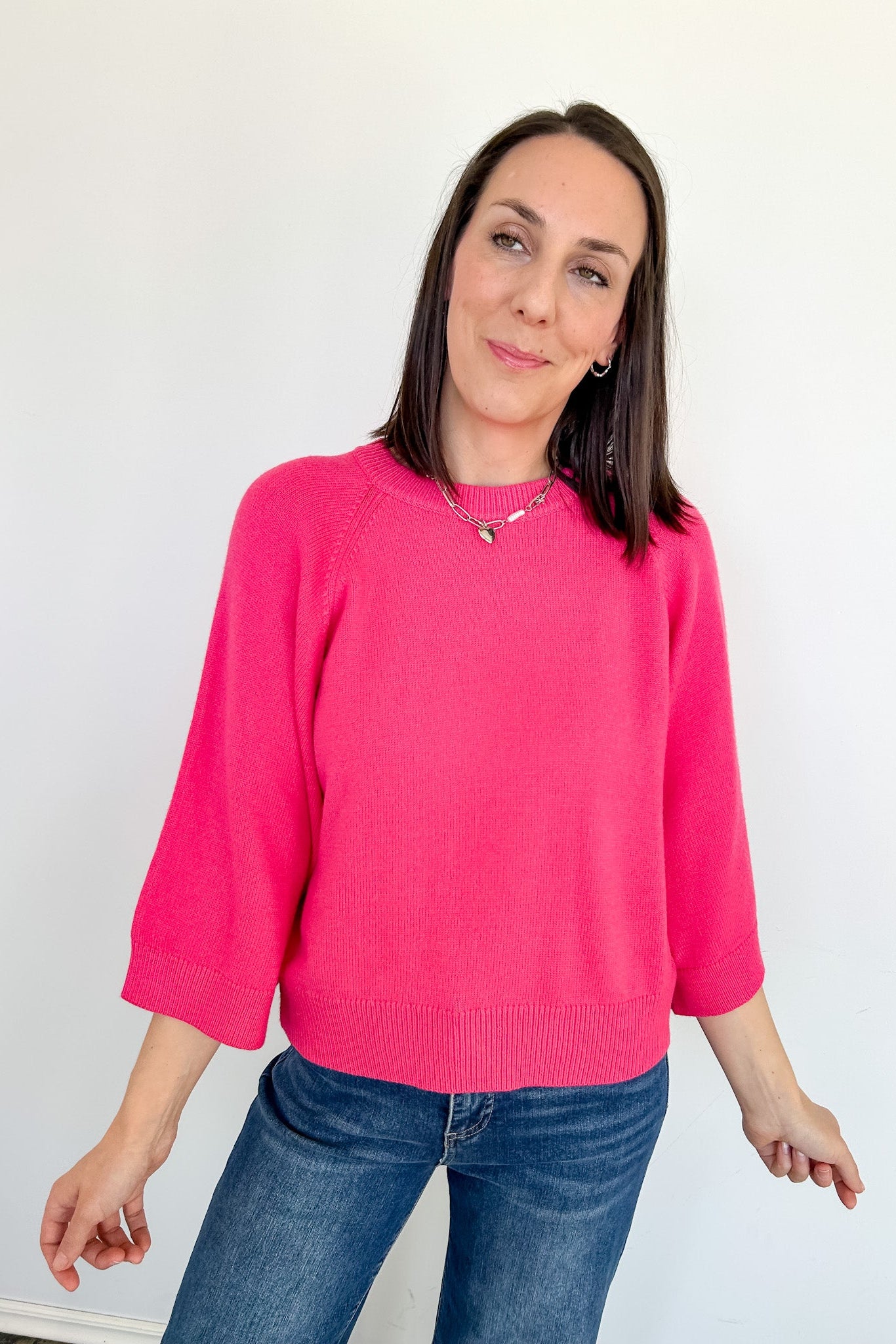 Woman wearing a bright pink sweater and blue jeans against a white background