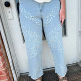 Person wearing light blue jeans and a white top standing in front of a door.