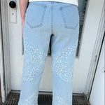 Person wearing light blue jeans with lace details standing in front of a door.