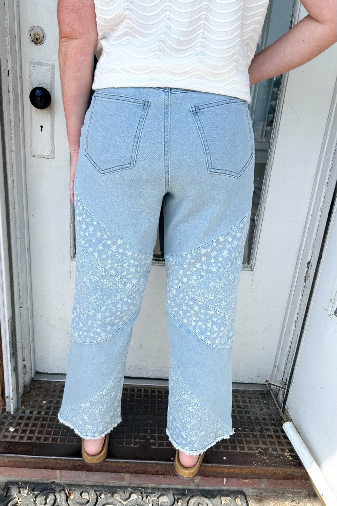 Person wearing light blue jeans with lace details standing in front of a door.