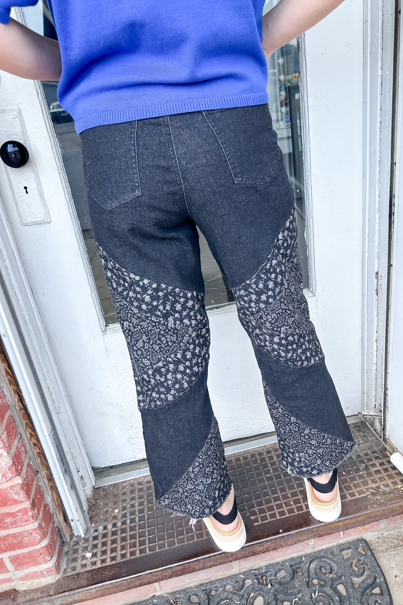 Person wearing blue sweater and patterned pants standing at a door.