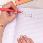Person writing in a notebook with a colorful pen on a light surface