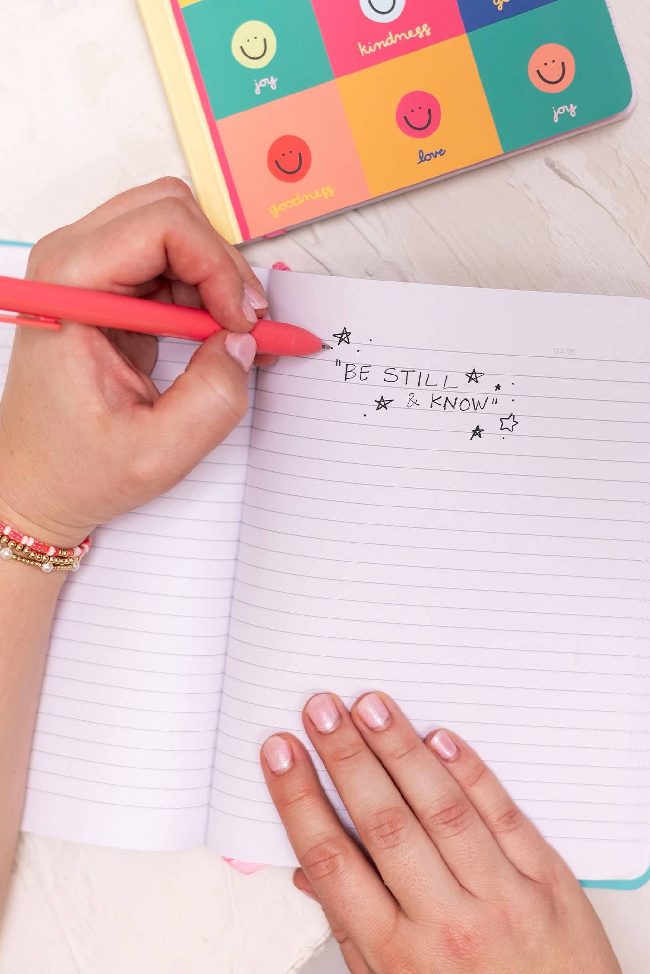 Person writing in a notebook with a colorful pen on a light surface