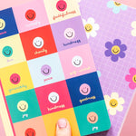 Colorful sticker sheets with smiley faces and motivational phrases on a pink background