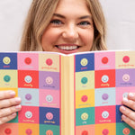 Woman holding a colorful checkered notebook with smiley faces on a plain background