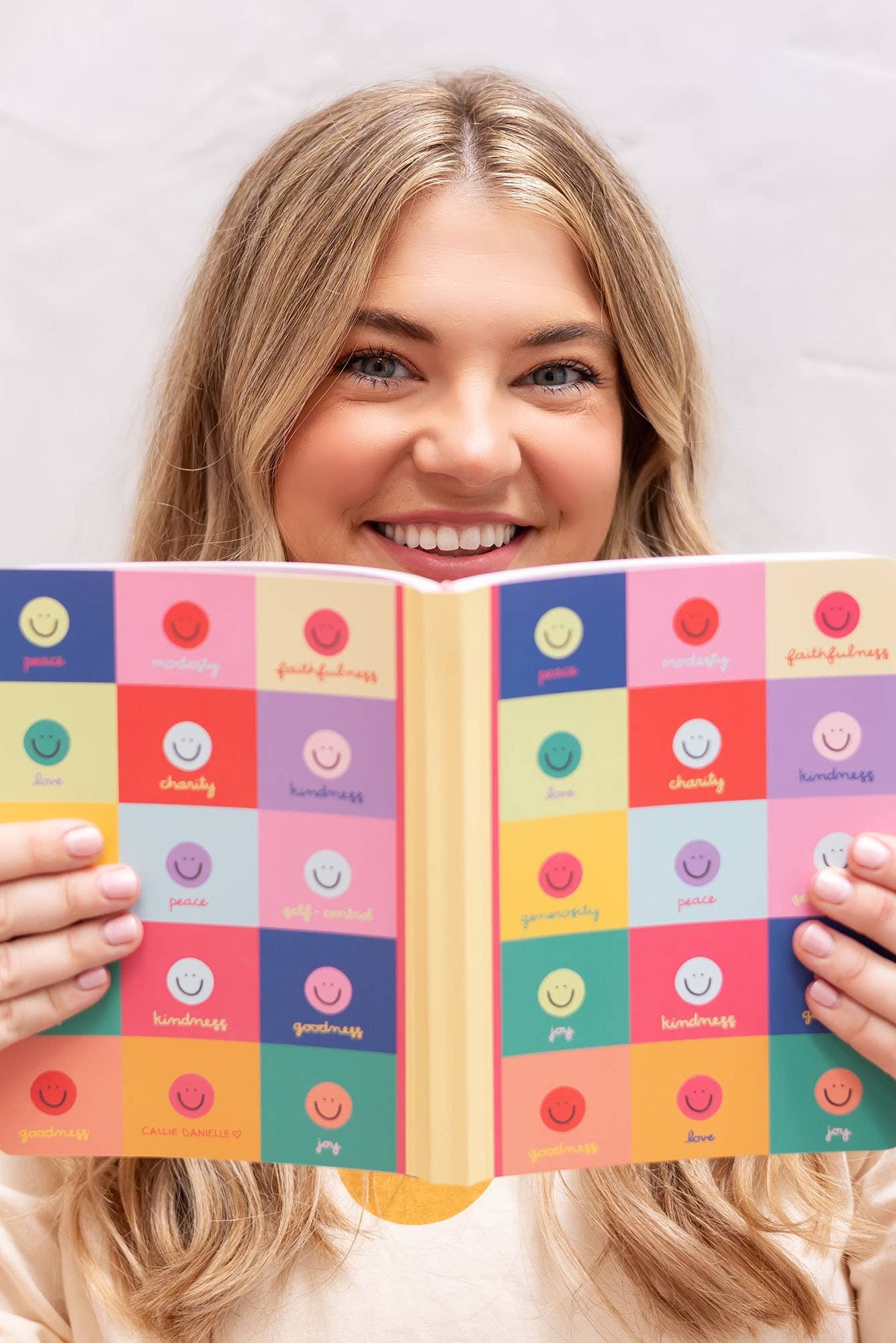 Woman holding a colorful checkered notebook with smiley faces on a plain background