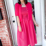 Woman in a bright pink dress standing in front of a door.
