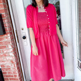 Woman in a bright pink dress standing in front of a door.