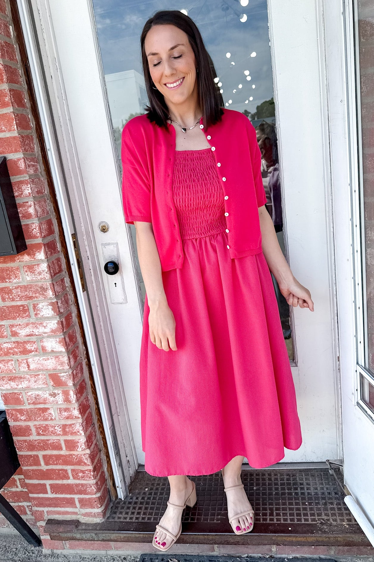 Woman in a bright pink dress standing in front of a door.