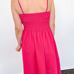 Person wearing a bright pink dress with thin straps against a white wall.