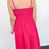 Person wearing a bright pink dress with thin straps against a white wall.