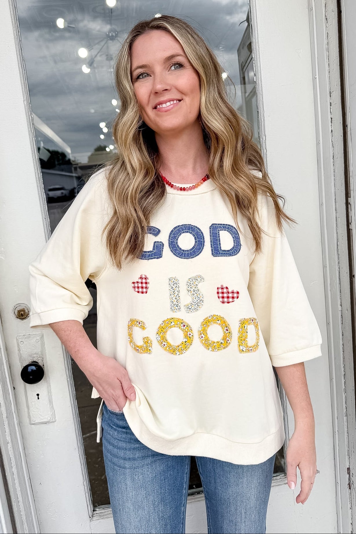 Woman wearing a 'GOD IS GOOD' shirt standing in front of a door.