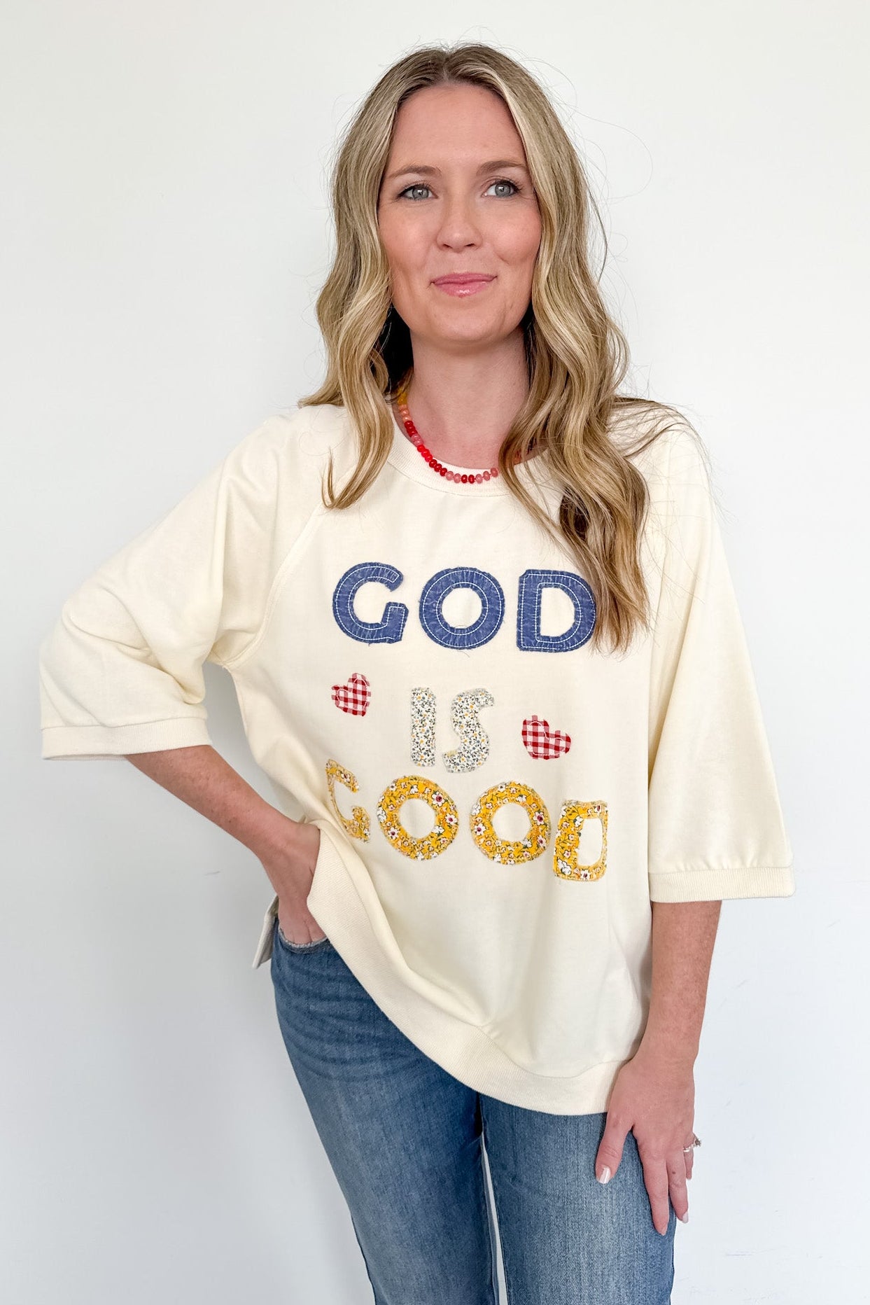 Woman wearing a cream-colored t-shirt with 'GOD IS GOOD' text on a white background