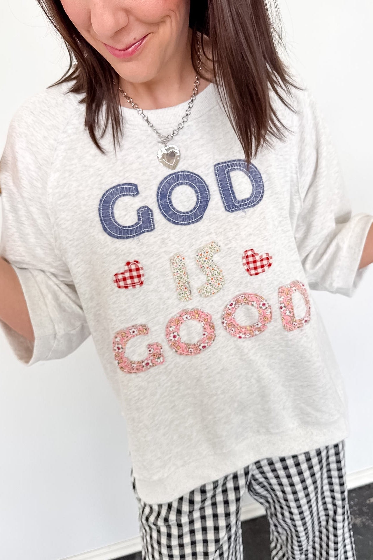 Person wearing a white t-shirt with 'GOD IS GOOD' text, standing indoors.