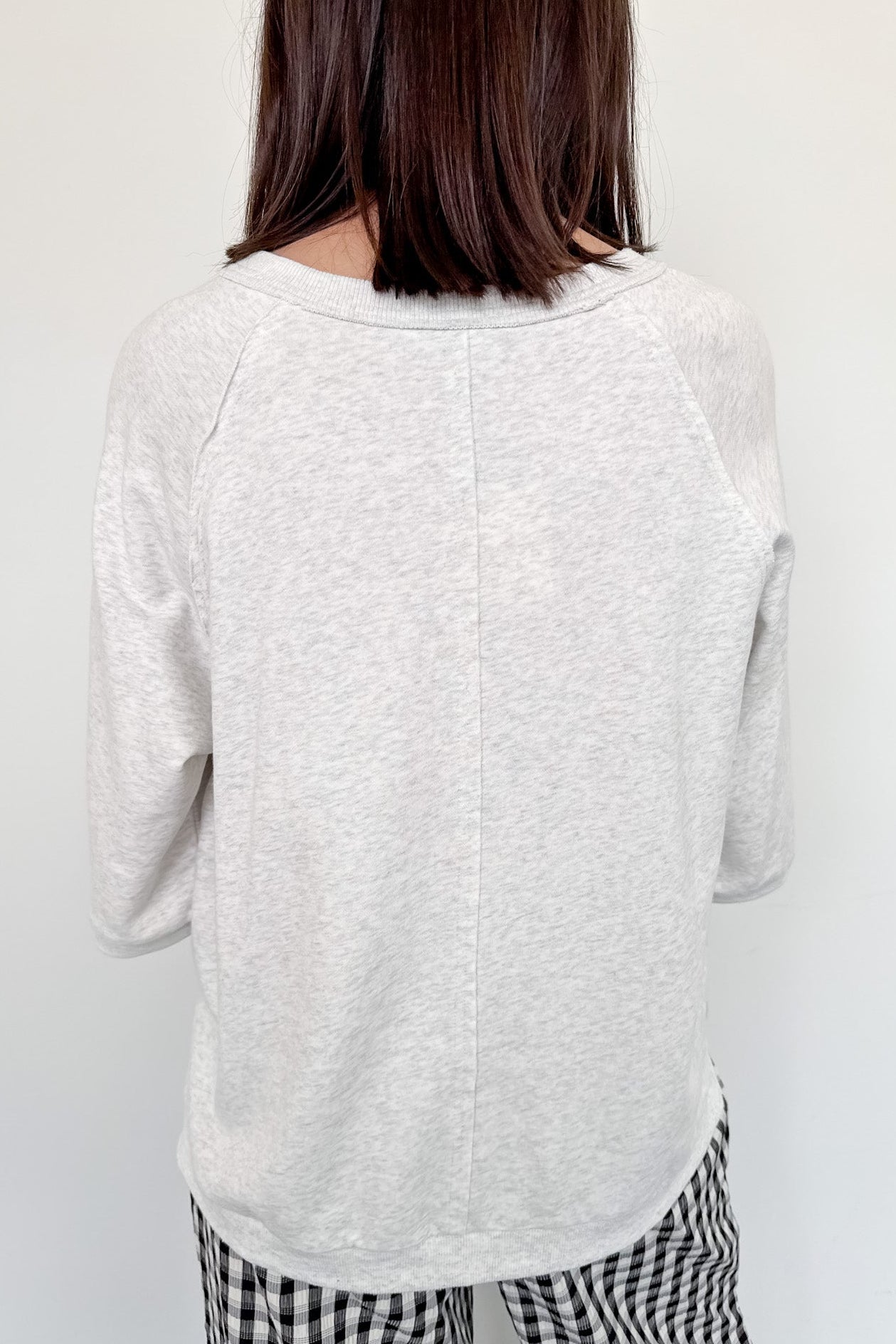 Person wearing a light gray sweater and checkered pants against a white wall