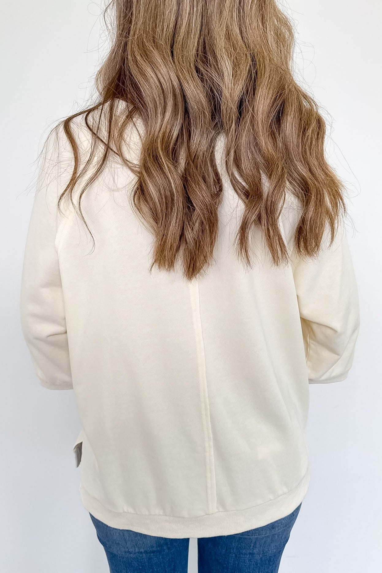 Person wearing a beige jacket and blue jeans against a white background