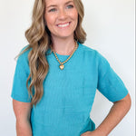 Woman wearing a blue sweater and heart-shaped necklace against a white background