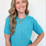Woman wearing a blue sweater and heart-shaped necklace against a white background