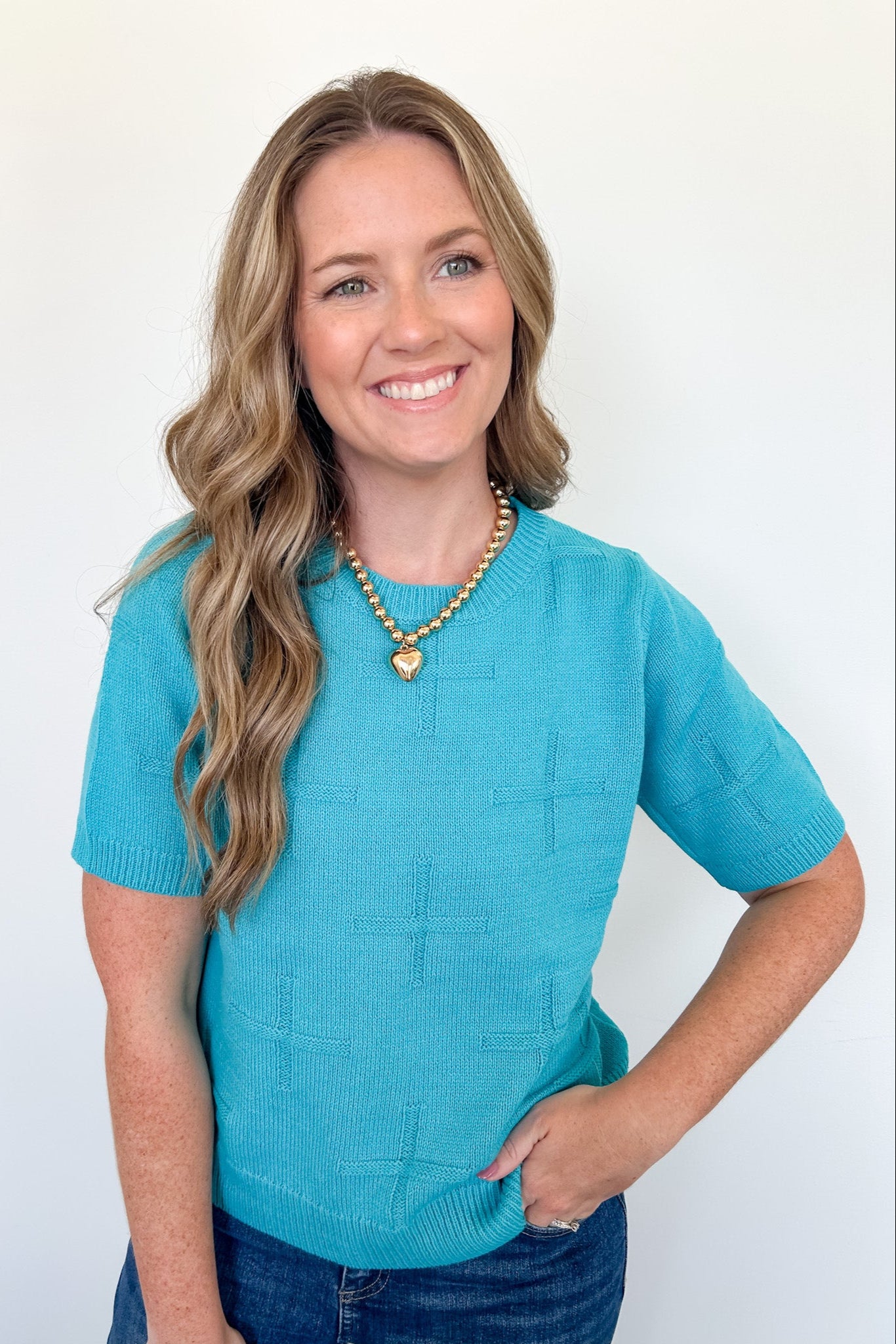 Woman wearing a blue sweater and heart-shaped necklace against a white background
