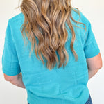 Person wearing a turquoise sweater with a plain background