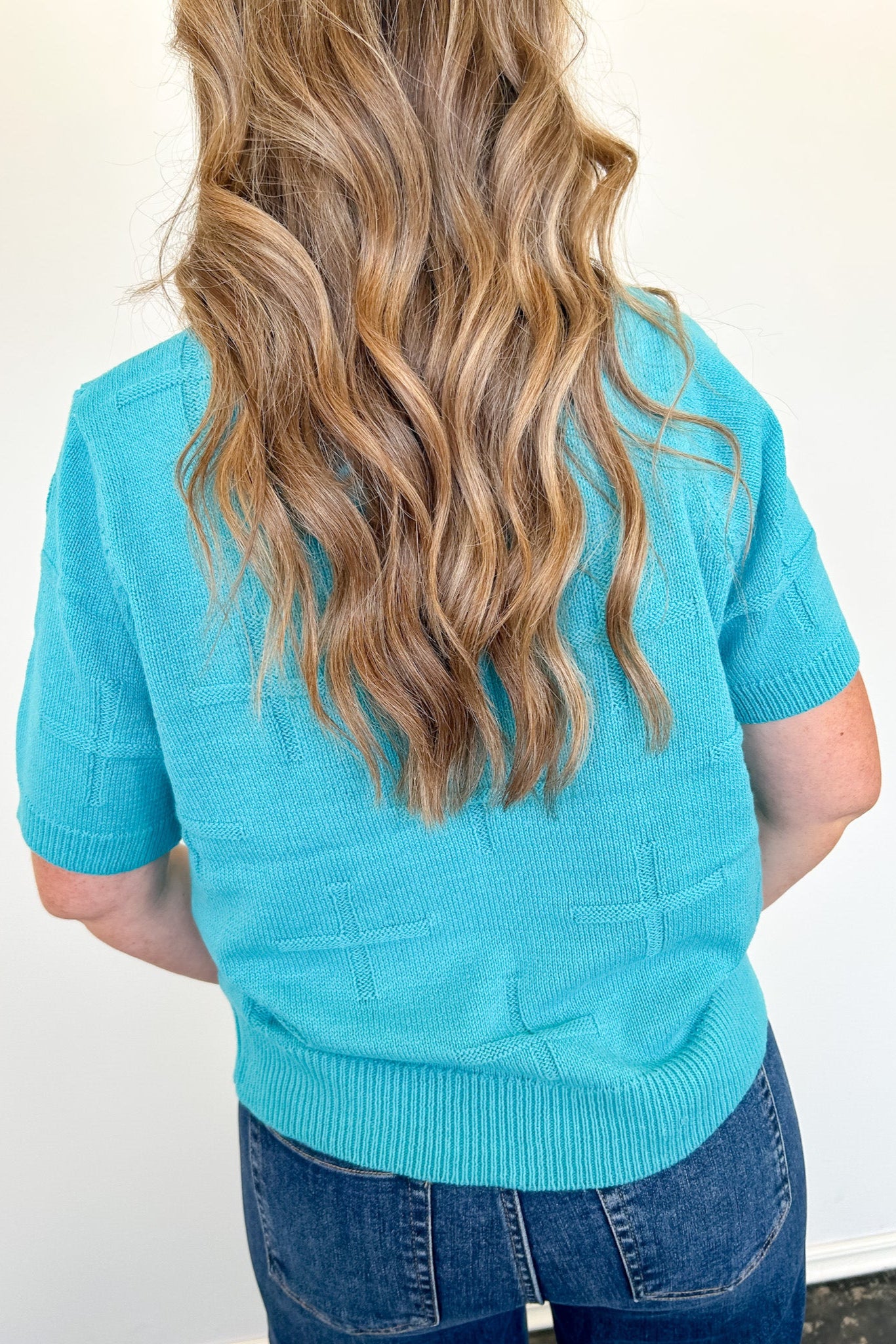 Person wearing a turquoise sweater with a plain background