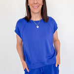 Woman wearing a blue outfit standing against a white wall.