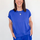 Woman wearing a blue outfit standing against a white wall.