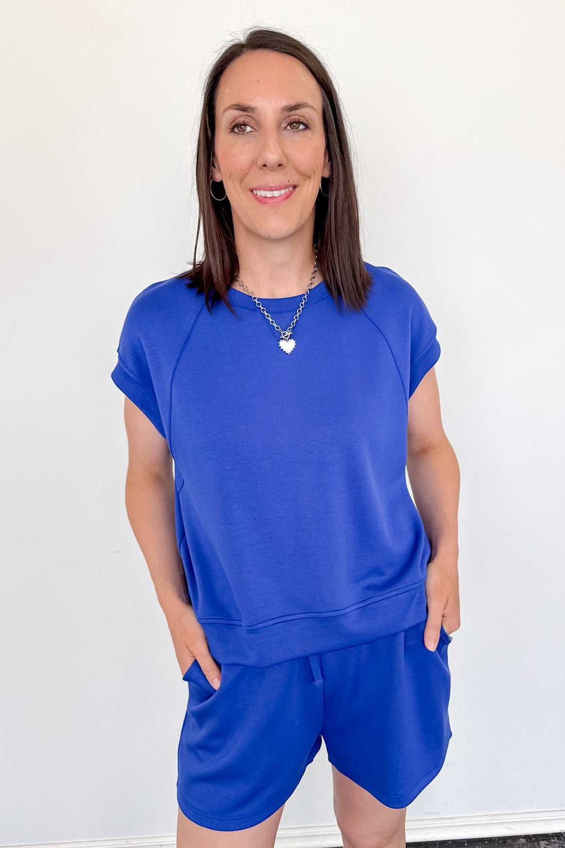 Woman wearing a blue outfit standing against a white wall.