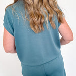Person wearing a teal outfit with shorts against a white wall