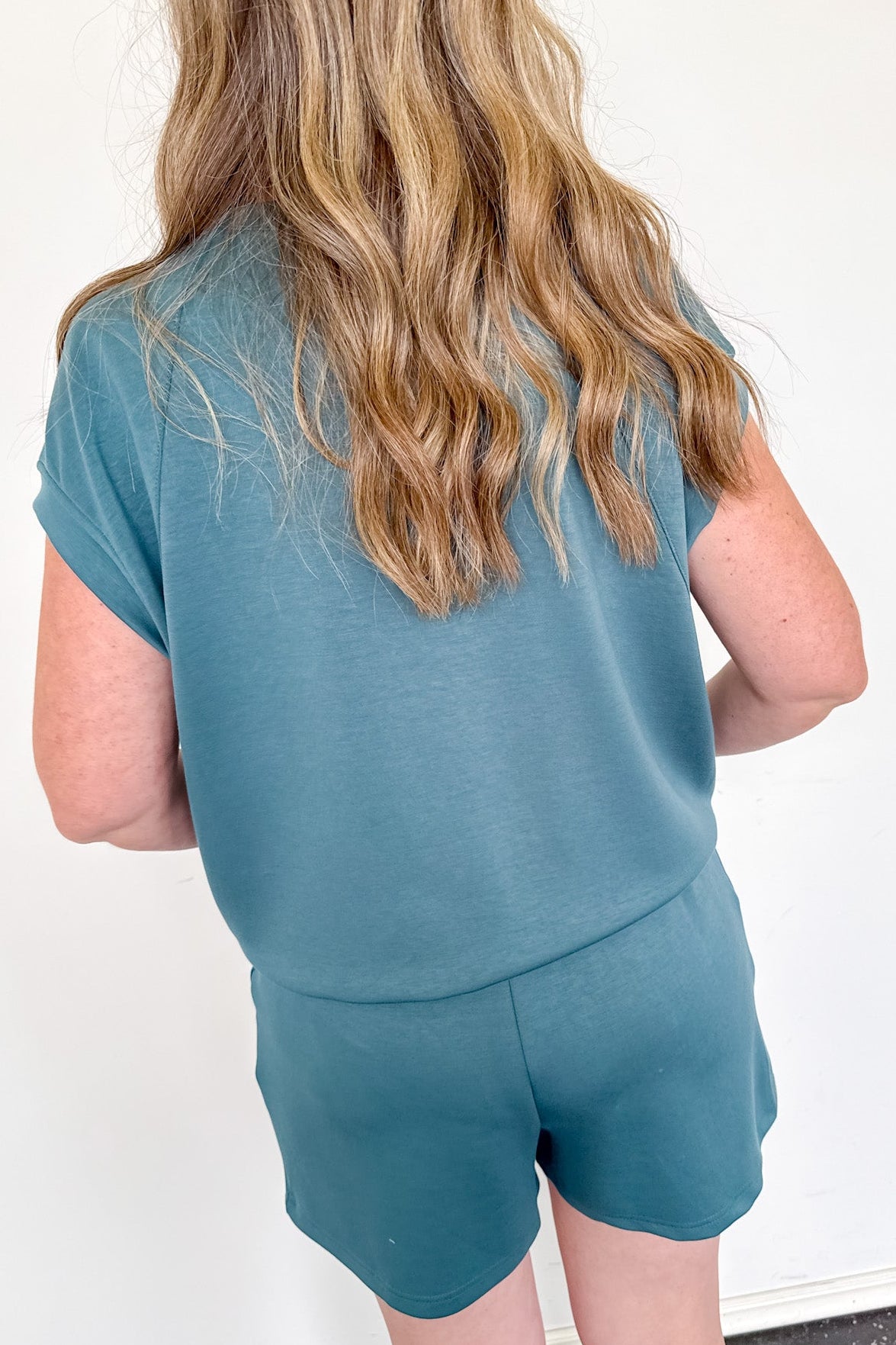 Person wearing a teal outfit with shorts against a white wall