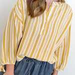 Person wearing a yellow and white striped blouse with blue jeans on a plain background