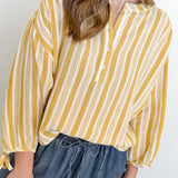 Person wearing a yellow and white striped blouse with blue jeans on a plain background