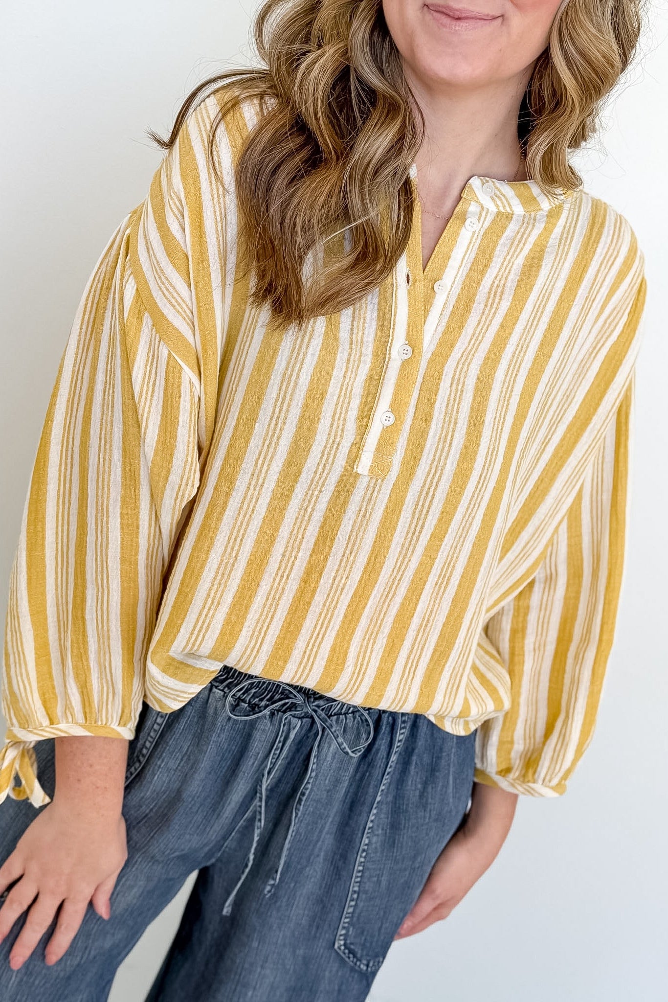 Person wearing a yellow and white striped blouse with blue jeans on a plain background