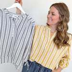 Woman holding a striped shirt on a hanger next to herself wearing a yellow and white striped shirt.