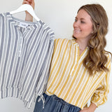 Woman holding a striped shirt on a hanger next to herself wearing a yellow and white striped shirt.